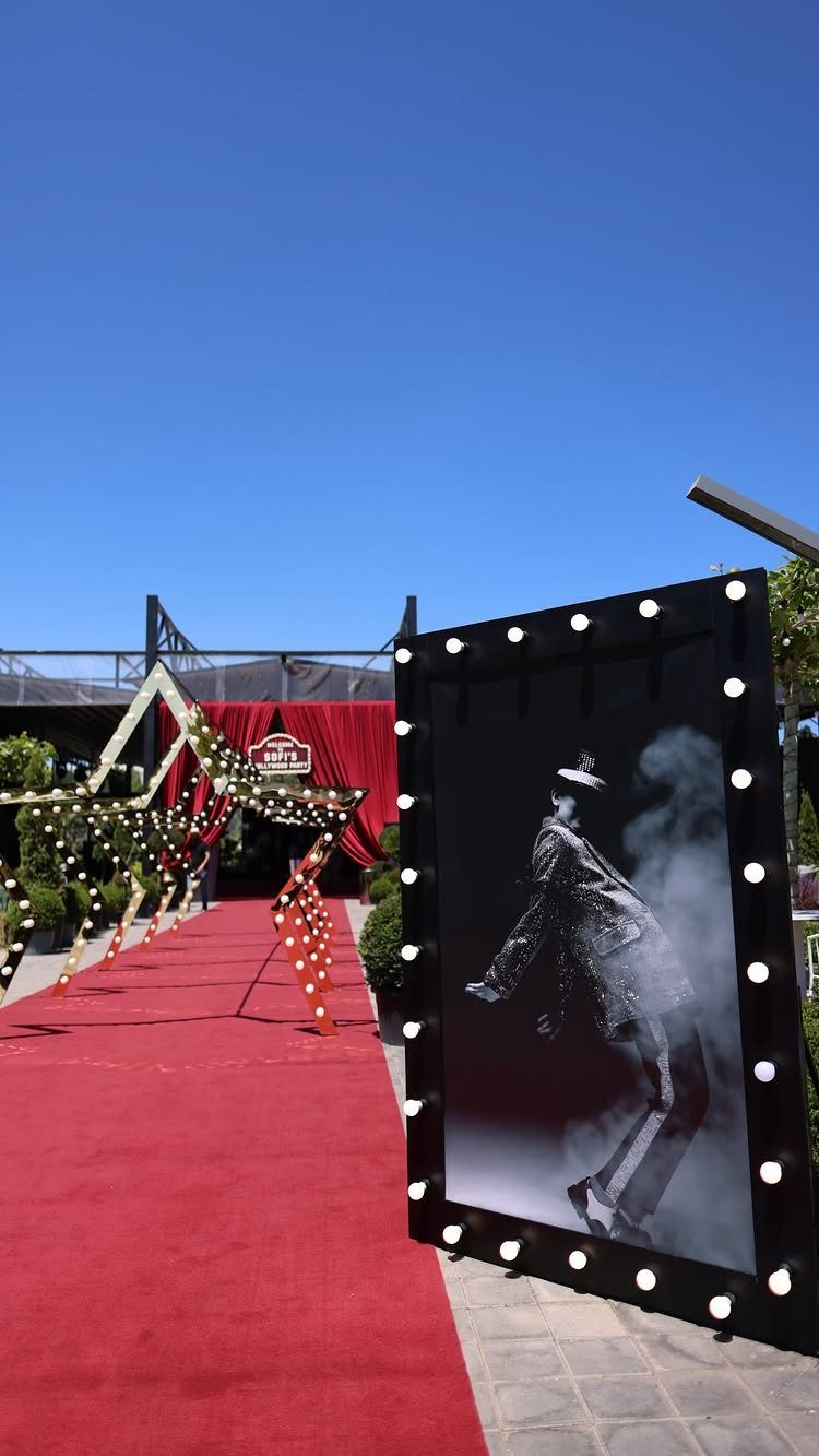 Red carpet entrance with a large illuminated movie-style portrait frame and string lights.