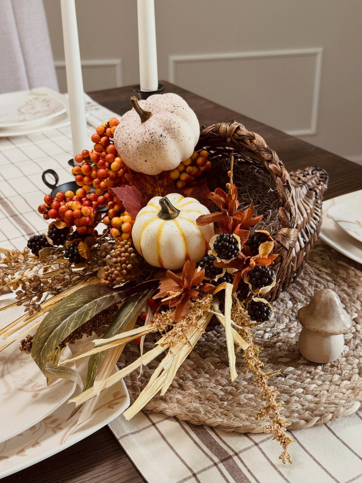 Woven cornucopia filled with mini white pumpkins, orange berries, and autumn foliage on a table.