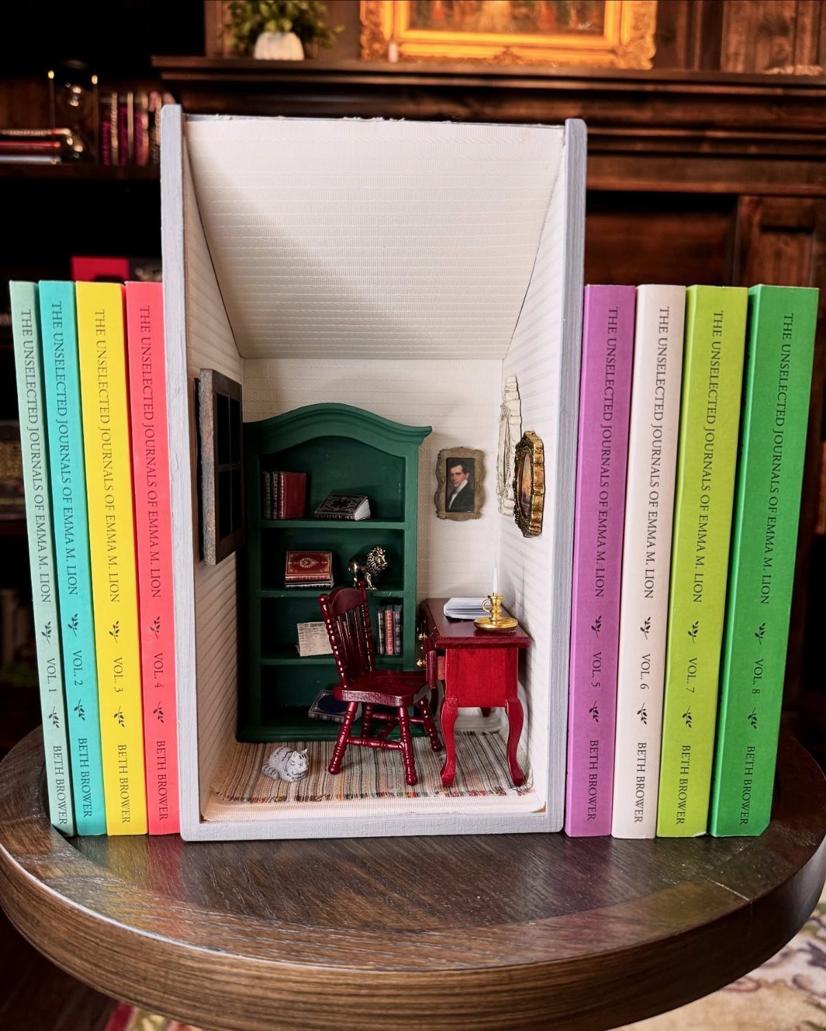 Miniature room diorama with red furniture placed between colorful books on a table.