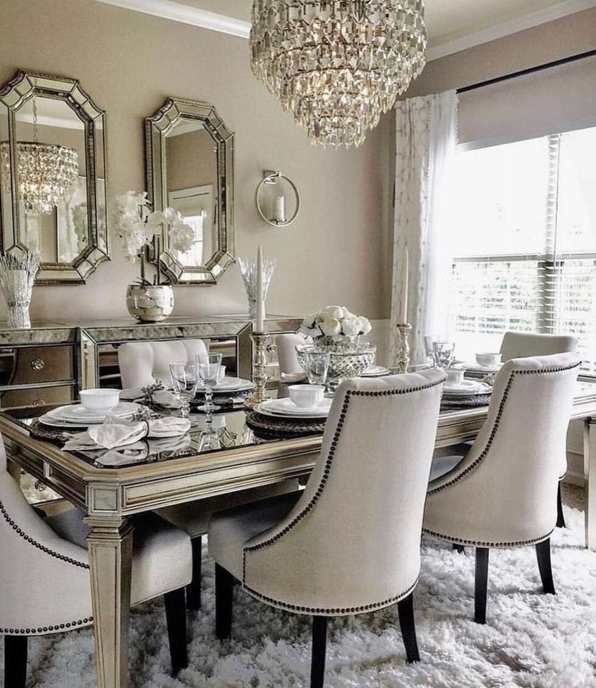 Mirrored dining table and wall mirrors in a glam room with crystal chandelier.