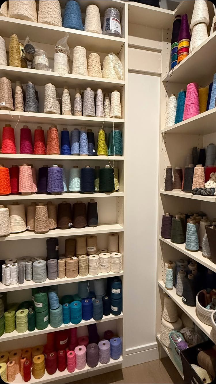 White wooden shelves stocked with colorful cones of yarn in a narrow space.