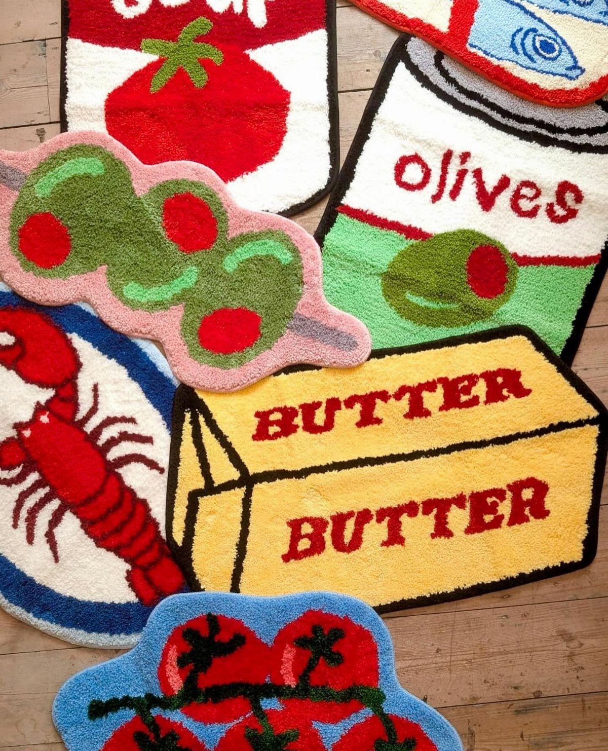 23 Cool House Items for Walls, Shelves, Desks, and Baths 15 Colorful tufted bath mats shaped like butter, lobster, and olives on wooden flooring.