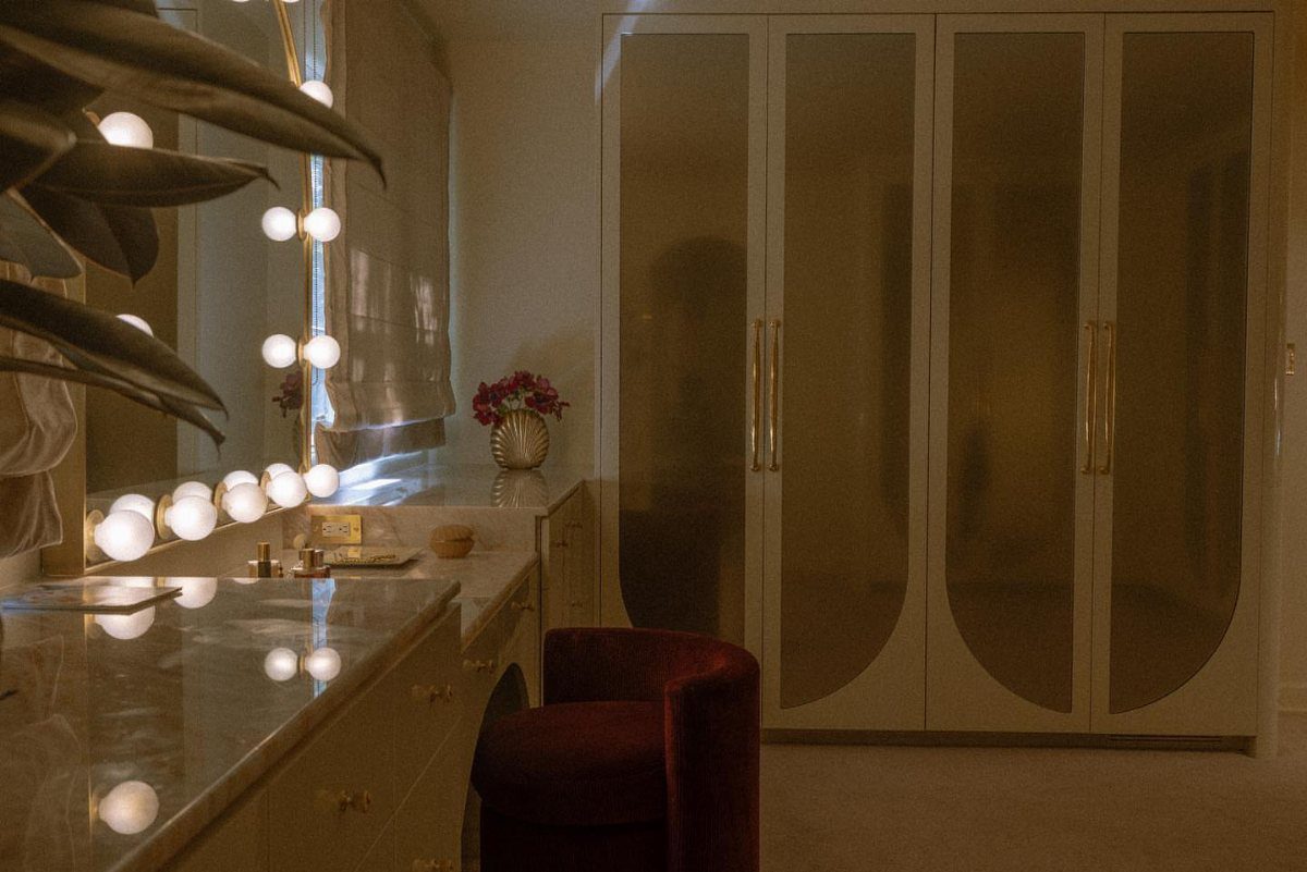 Luxurious dressing room with marble vanity, globe lights, and red velvet chair.