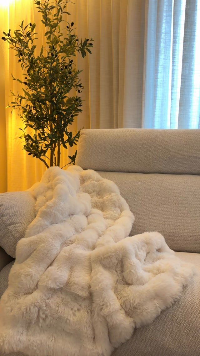 White faux-fur oversized throw blanket draped over a light grey fabric sofa