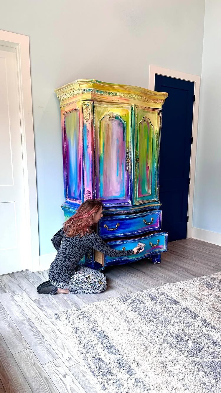 Rainbow painted ornate armoire with a woman opening one of its drawers.