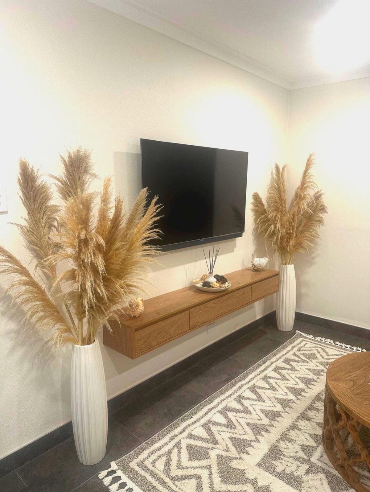 40 Home Decor Item Ideas, From Candle Holders to Sculptures 5 Pampas grass in white vases flanking a wall-mounted wooden console and television.