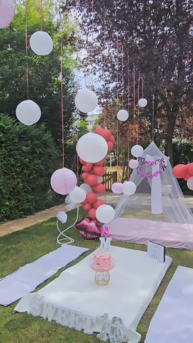 Outdoor birthday party setup with pink and white lanterns, balloons, and a teepee.