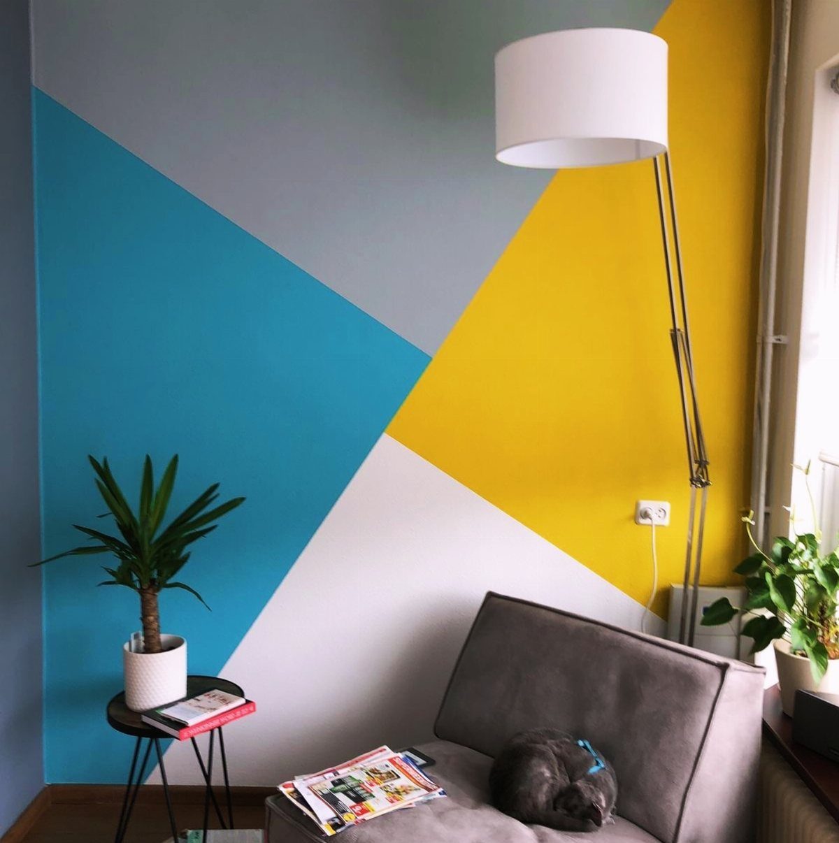 22 Bedroom Empty Wall Ideas, from Gallery Walls to Plaster 16 Wall painted with bold blue, yellow, grey, and white geometric shapes in a room.