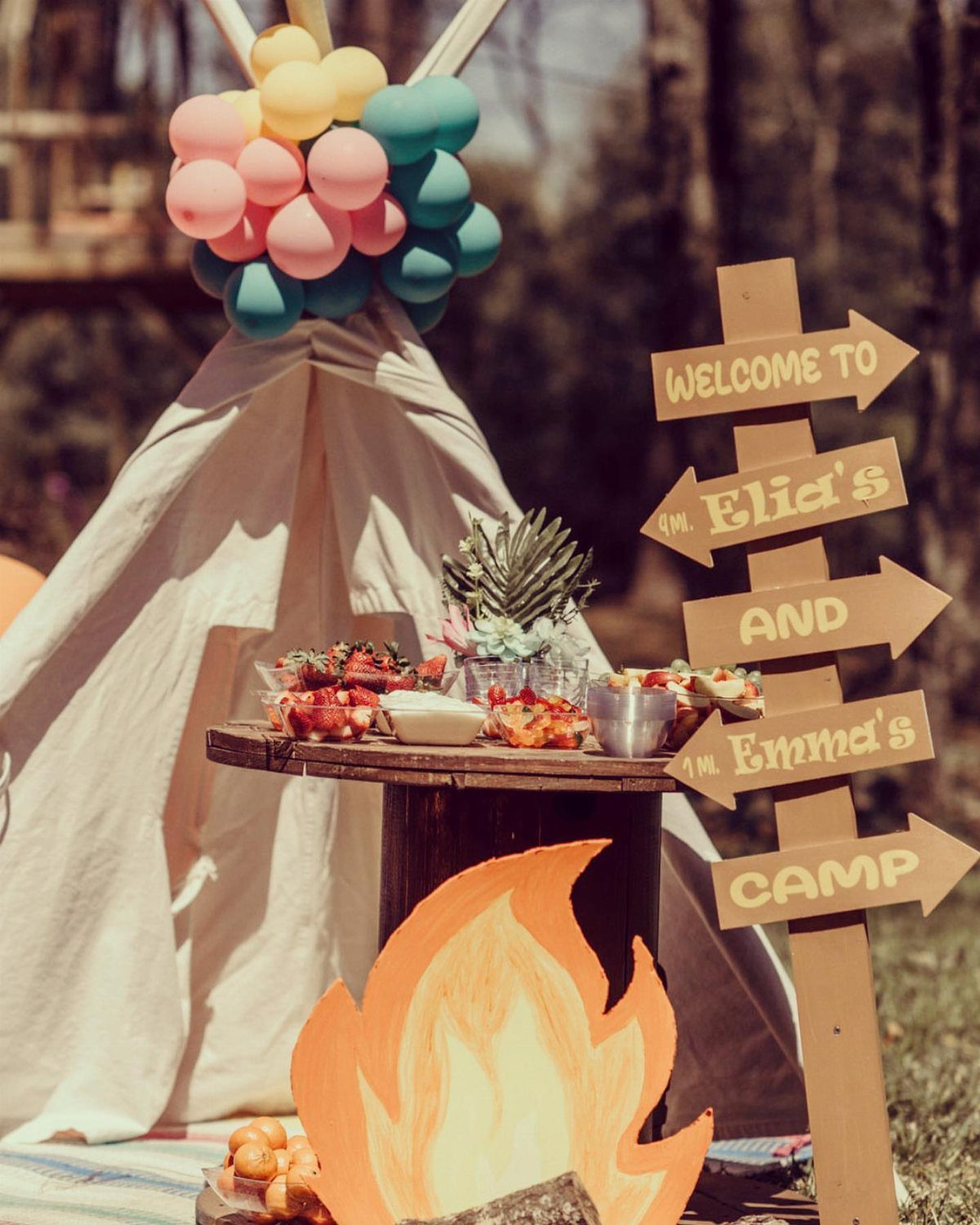 White teepee tent with colorful balloons and a wooden camp sign in a forest