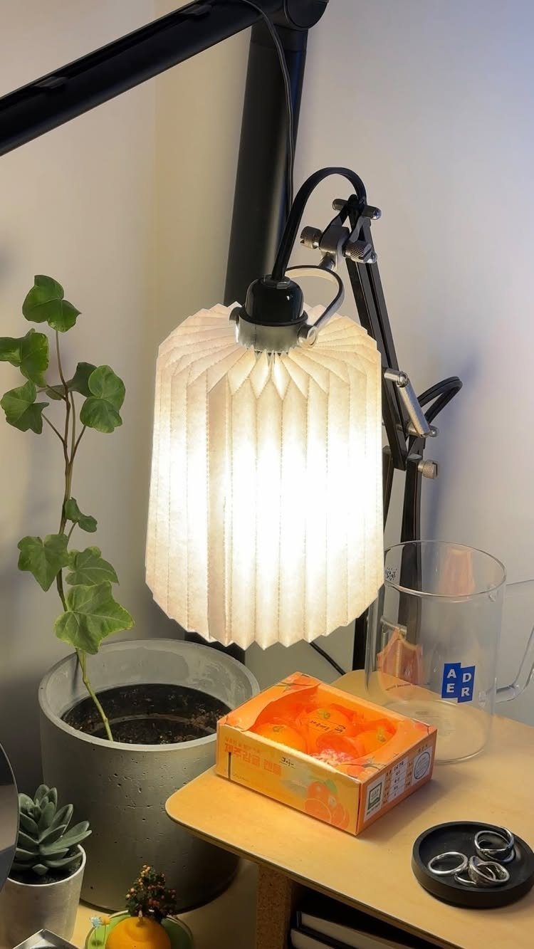 Make Table Lamp Ideas: 14 Designs in Wood, Glass and Ceramic 5 White pleated fabric lampshade on a black adjustable desk lamp next to a plant.