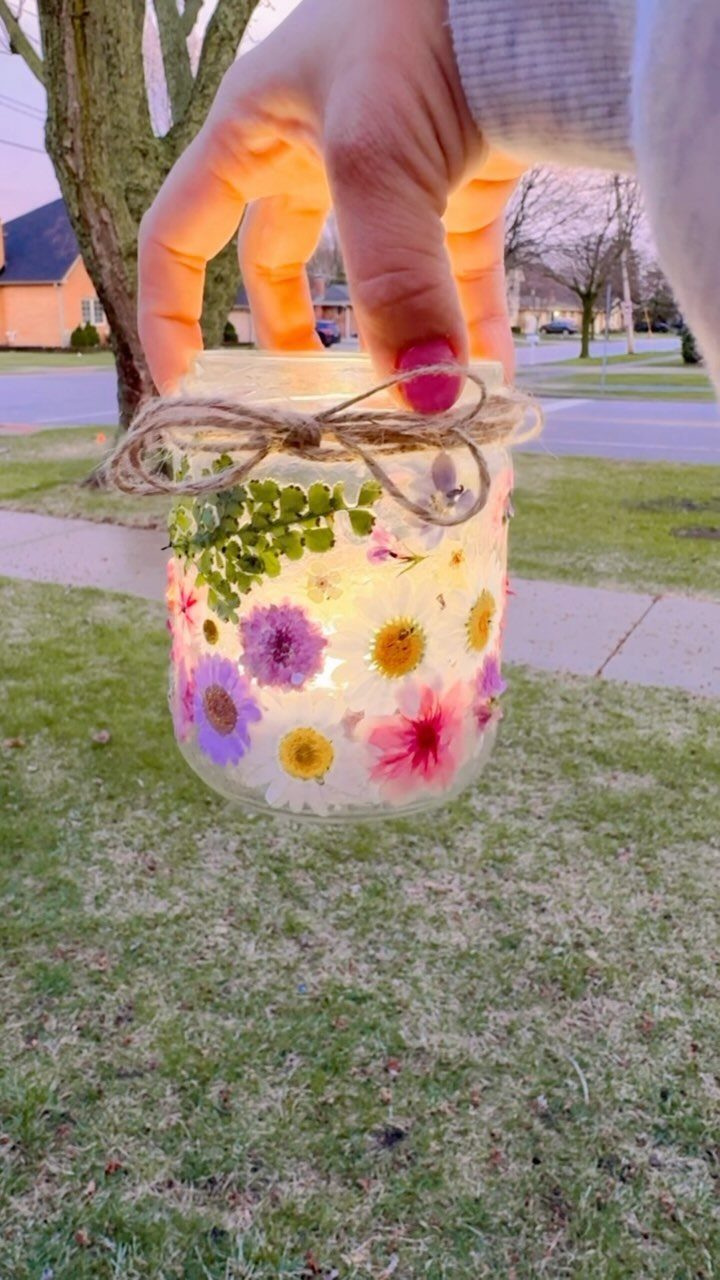 Glass jar with pressed flowers and fairy lights held over a green lawn