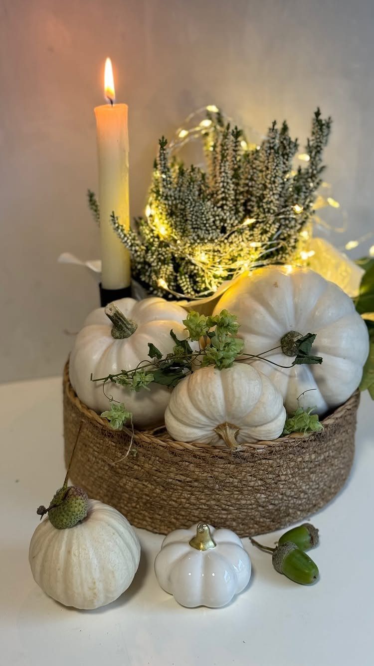 White pumpkins in a woven basket with a lit candle and fairy lights.