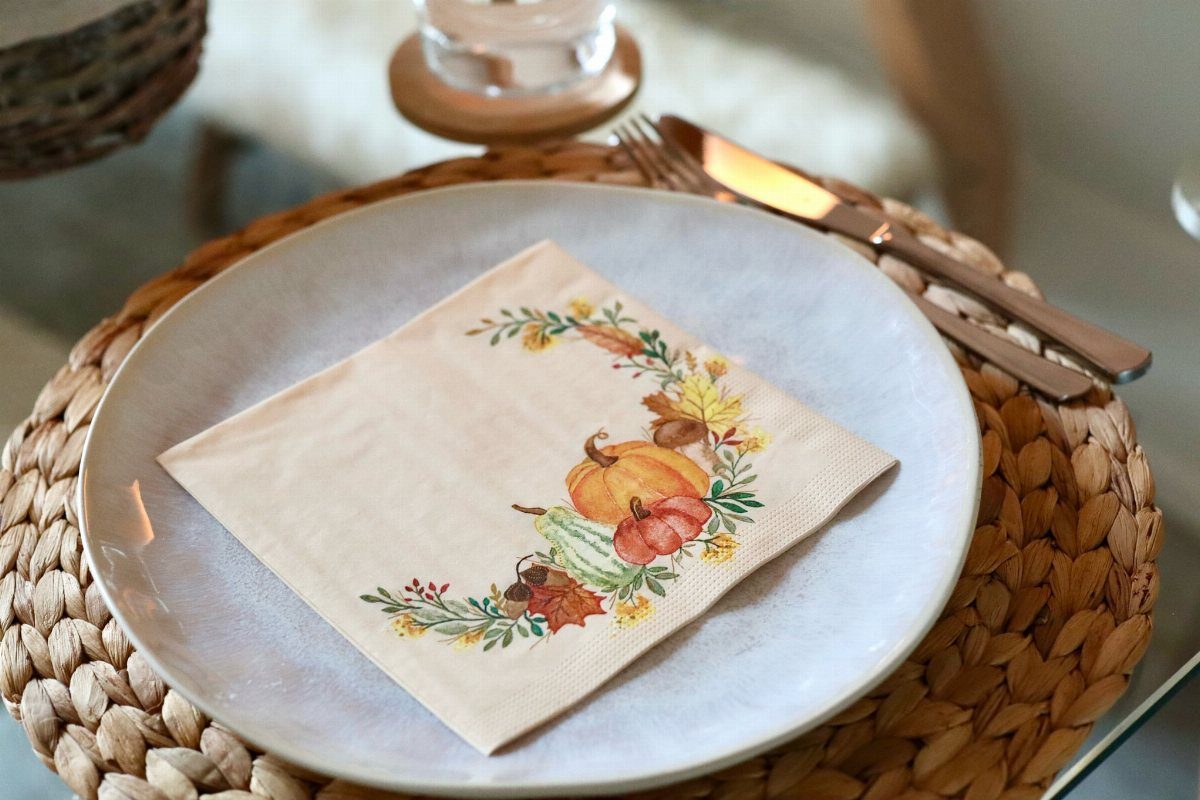Place setting with a pumpkin illustrated napkin on a white plate and woven charger.