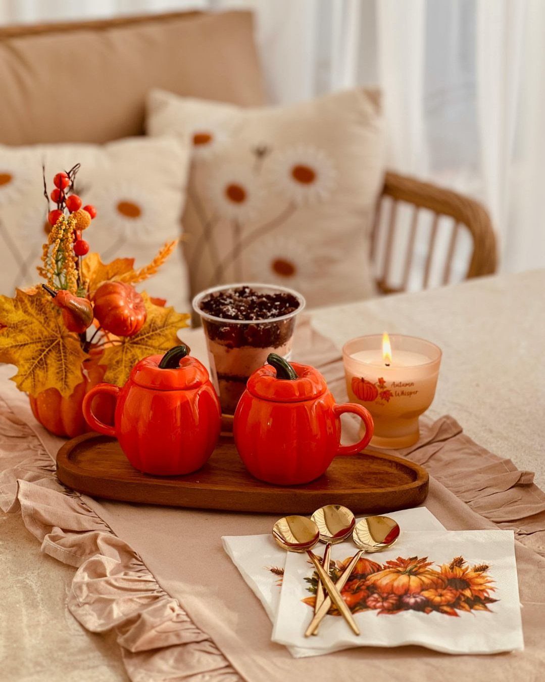Pumpkin shaped mugs and autumn decorations arranged on a ruffled beige table runner.