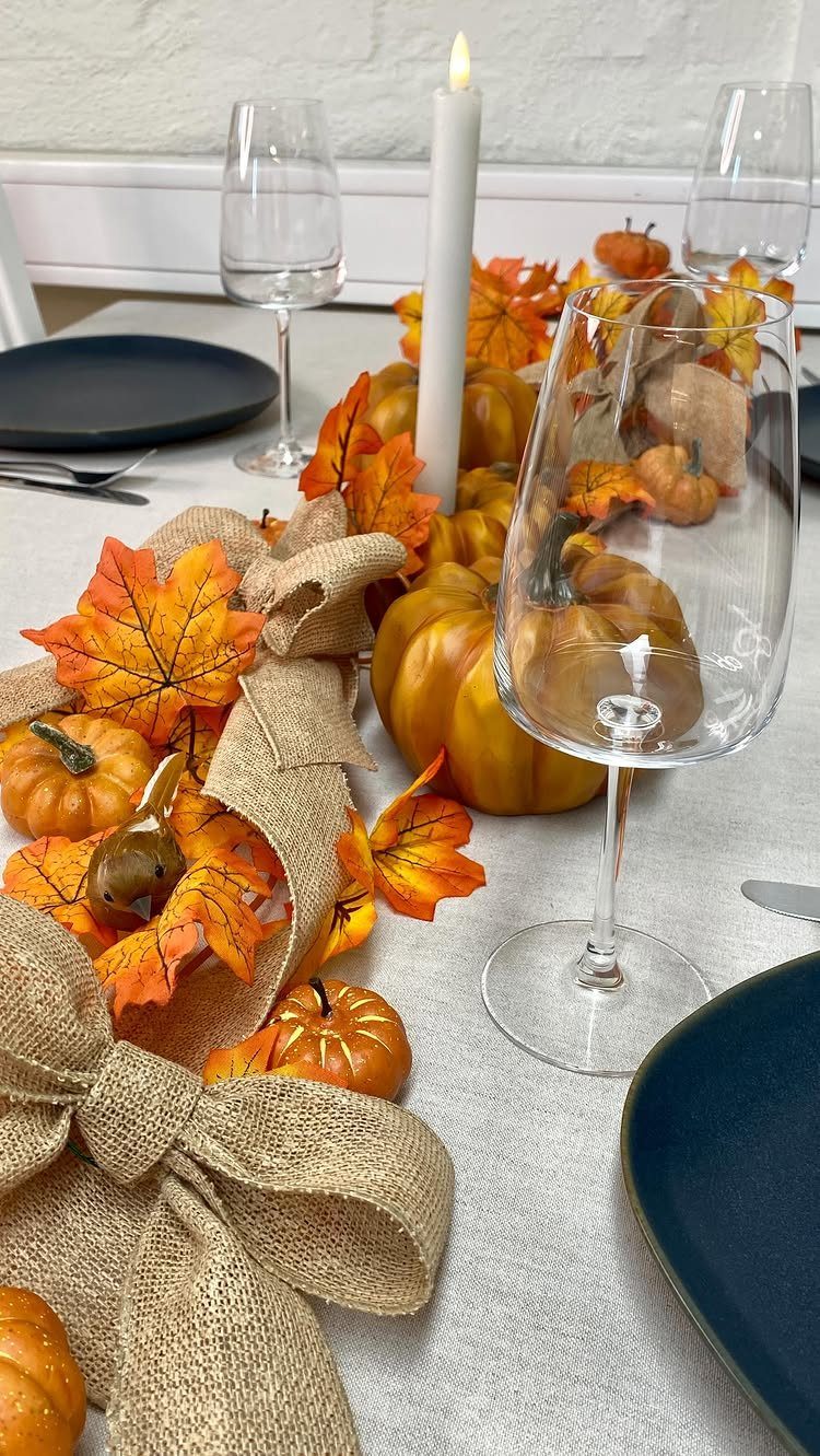 Autumn table setting with orange pumpkins, fall leaves, burlap ribbon, and white candle.
