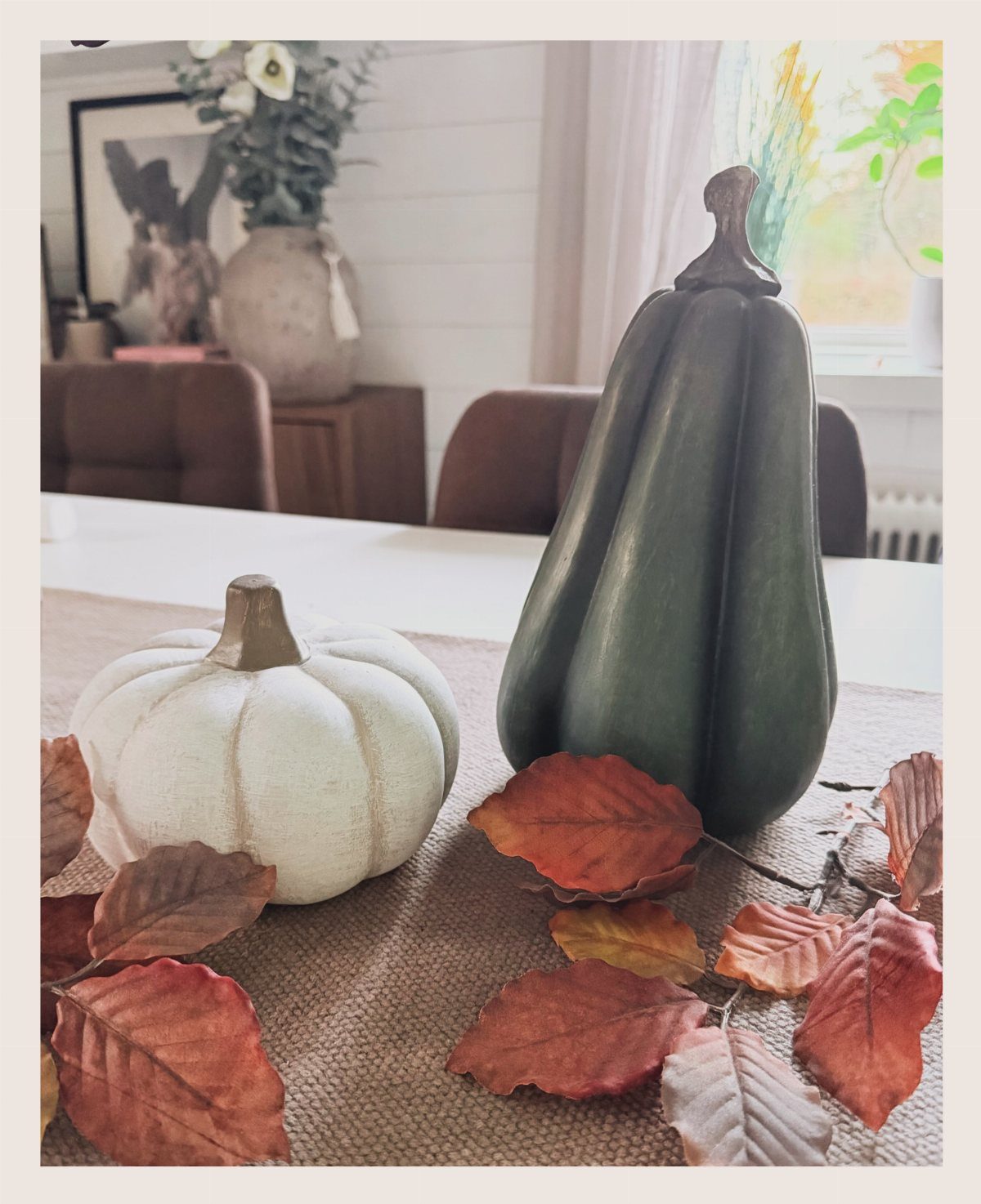 White pumpkin and green gourd with autumn leaves on a brown table runner