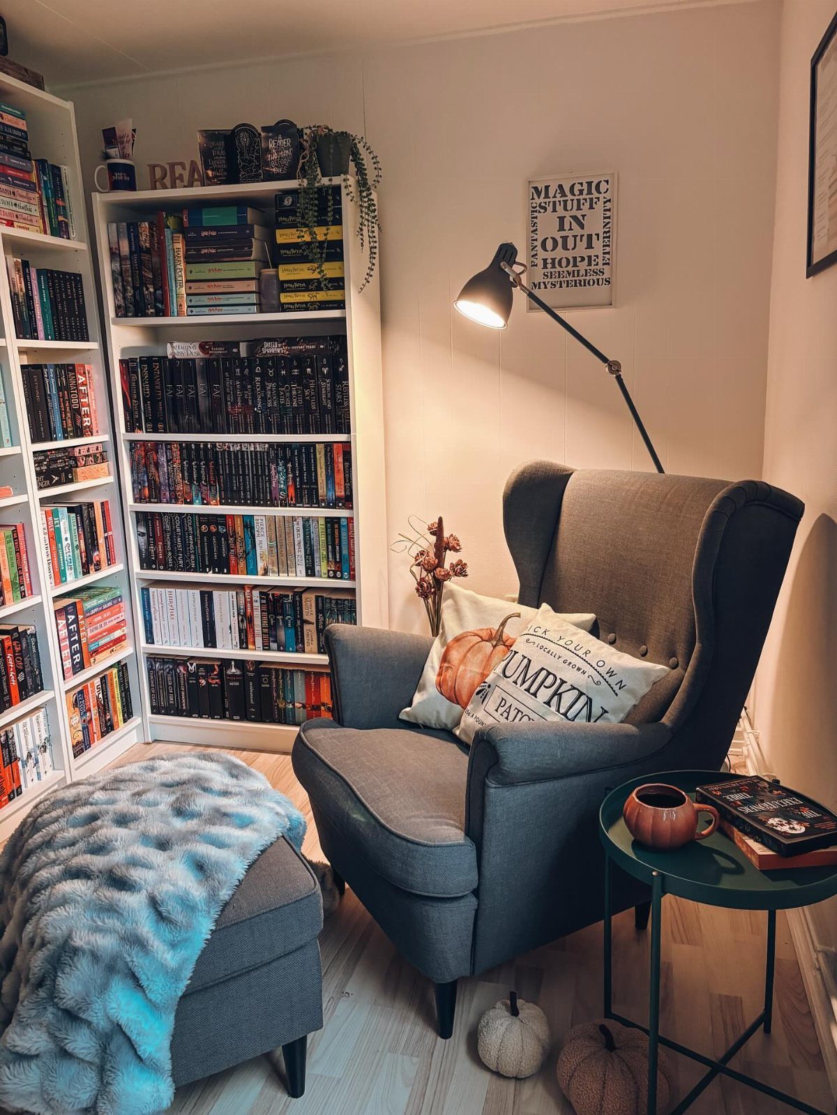 Grey wingback chair and blue ottoman next to tall white bookshelves filled with books.
