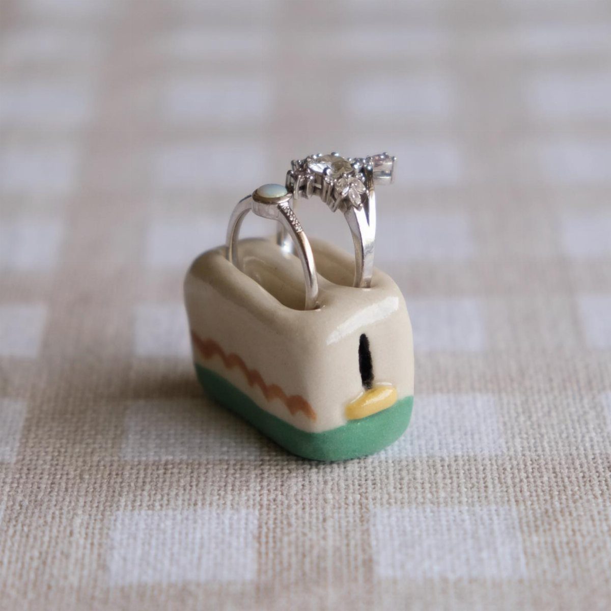 30 DIY Clay Crafts to Make with Air-Dry Clay for Home Decor 1 Small clay house ring holder with two silver diamond rings on checkered fabric.