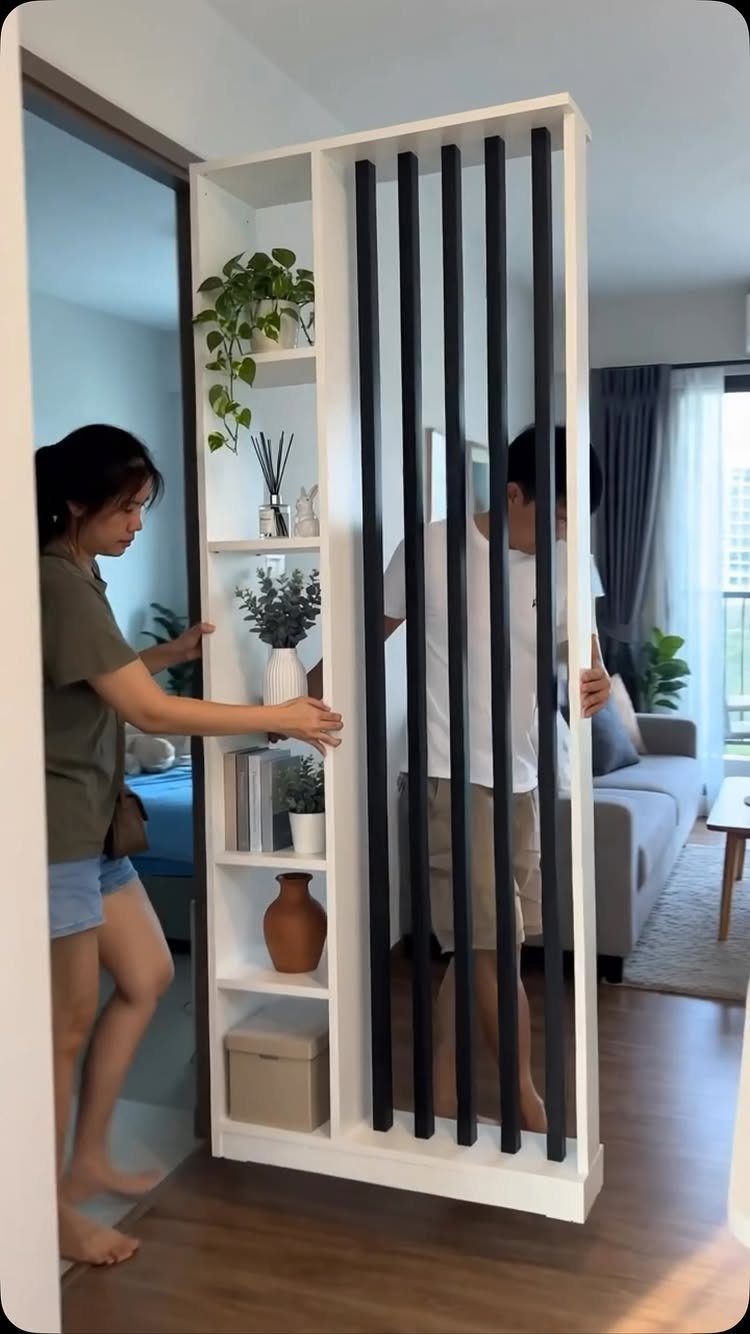 White open shelving unit with black slats acting as a room divider with plants.