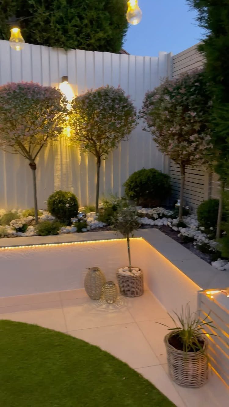 13 Rope Lighting Ideas Outdoor for Decks, Steps and Fences 7 Modern outdoor patio with warm rope lighting along a low white wall and garden.