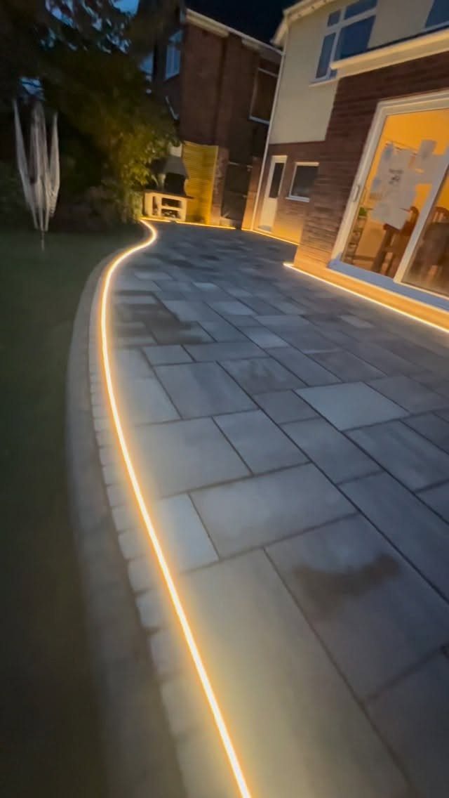 13 Rope Lighting Ideas Outdoor for Decks, Steps and Fences 10 Curved stone walkway with warm yellow rope lighting along the edge at dusk.