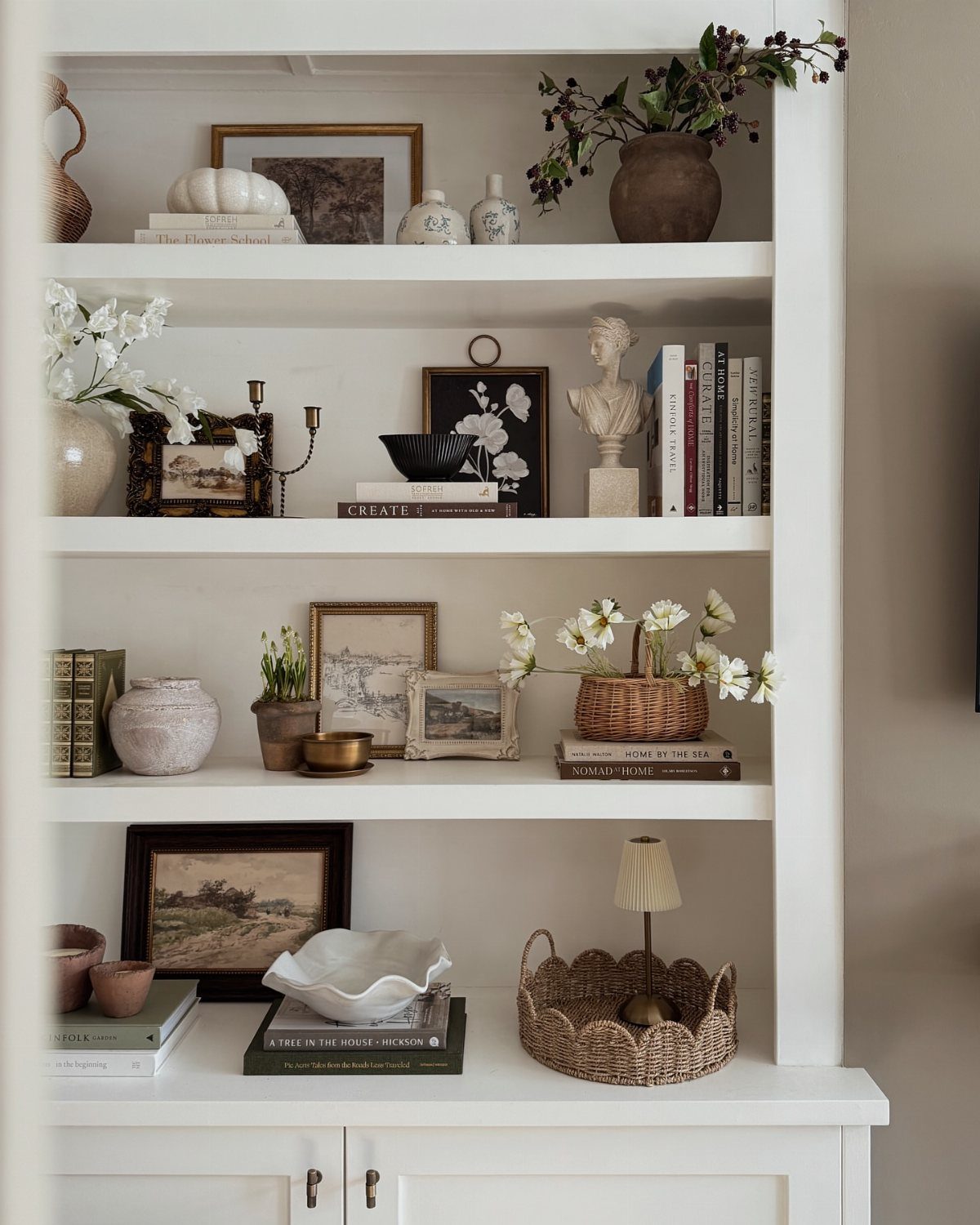 White built-in bookshelf styled with books, framed art, plants, and neutral ceramic decor.