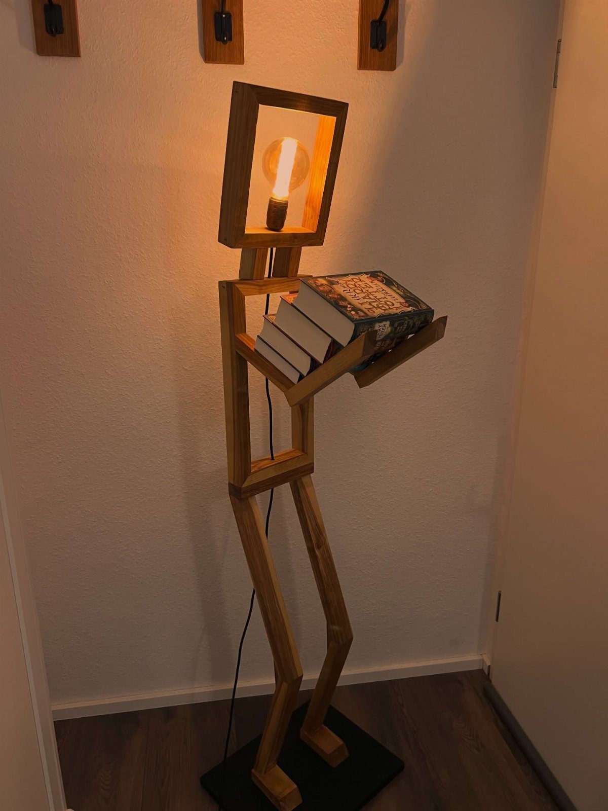 17 Handmade Lamps Ideas Using Wood, Concrete, and Glass Jars 3 Humanoid wooden floor lamp with a glowing bulb head and books on a shelf