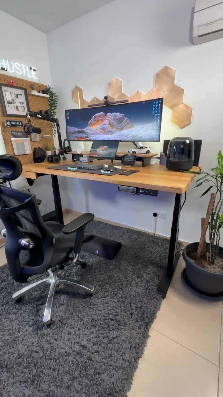 Wooden sit-stand desk with wide monitor, ergonomic chair, and grey shag rug.