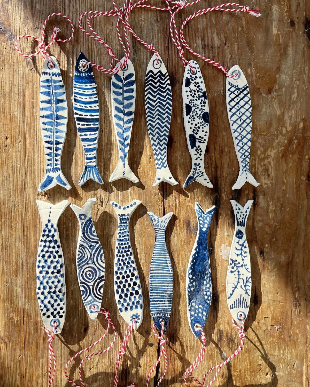 30 DIY Clay Crafts to Make with Air-Dry Clay for Home Decor 23 Handmade blue and white clay fish ornaments with red strings on a wooden background.
