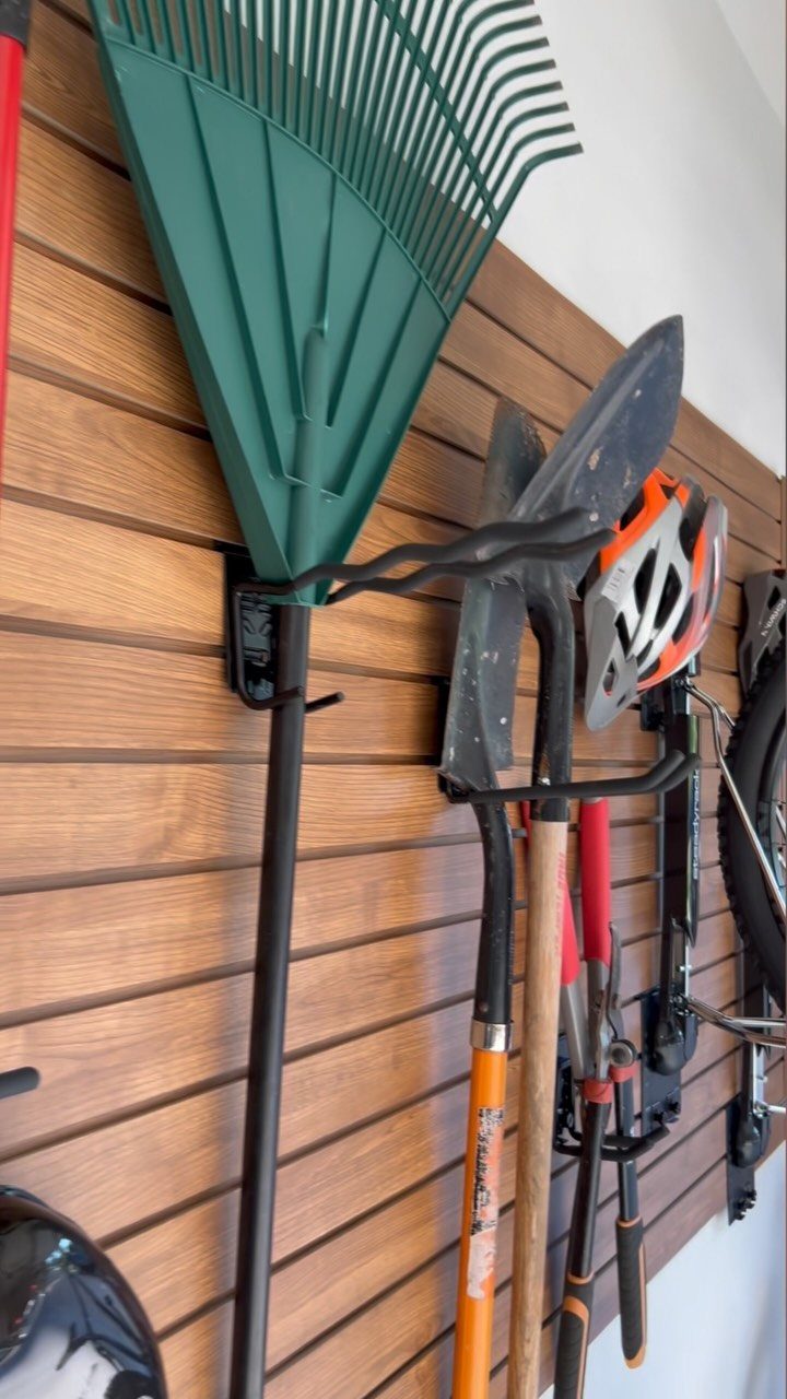 Garden tools and a bicycle organized on a brown wooden slatwall panel.