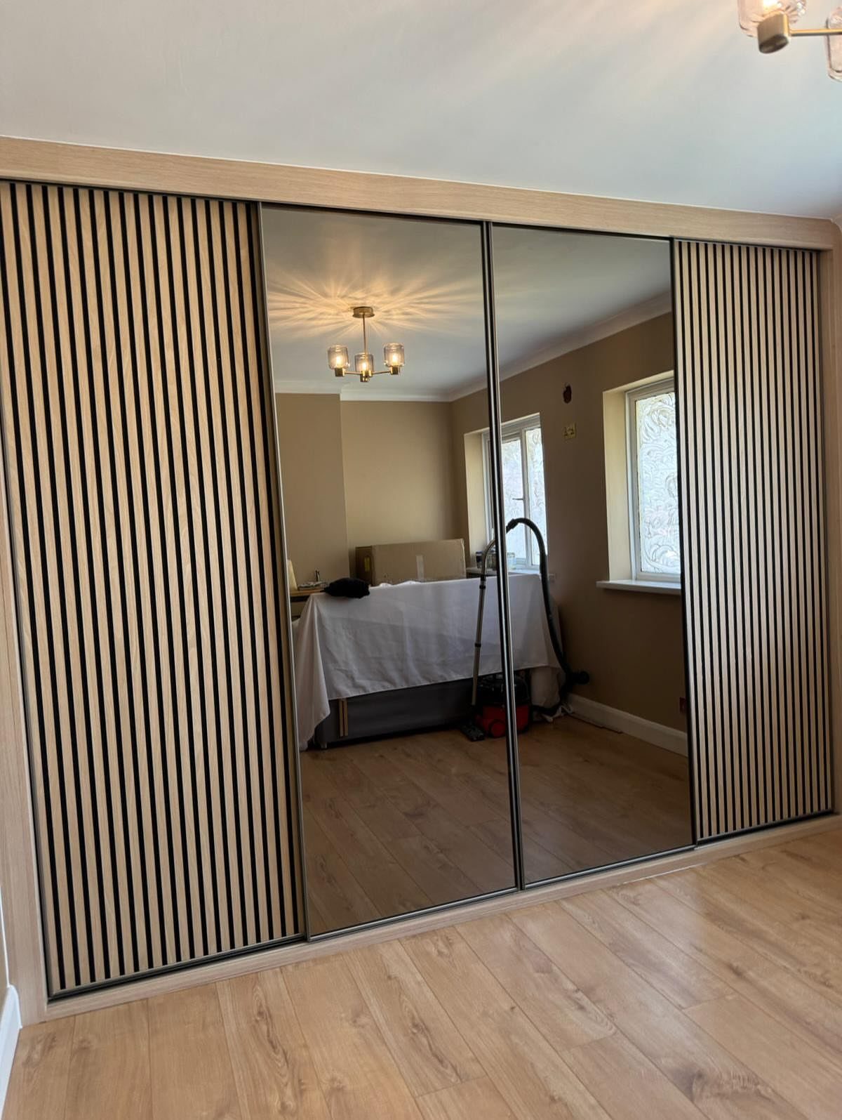 Sliding closet doors with central mirrored panels and outer vertical wood slat panels.