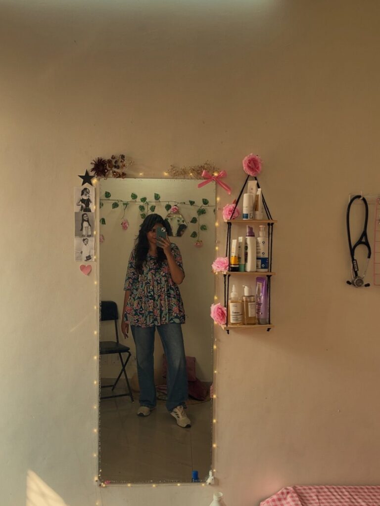 Full-length bedroom mirror decorated with fairy lights and flowers next to a skincare shelf.