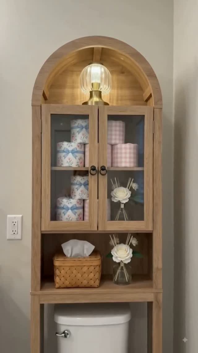 40 Home Decor Item Ideas, From Candle Holders to Sculptures 24 Light wood farmhouse storage cabinet with glass doors and arched top over a toilet.