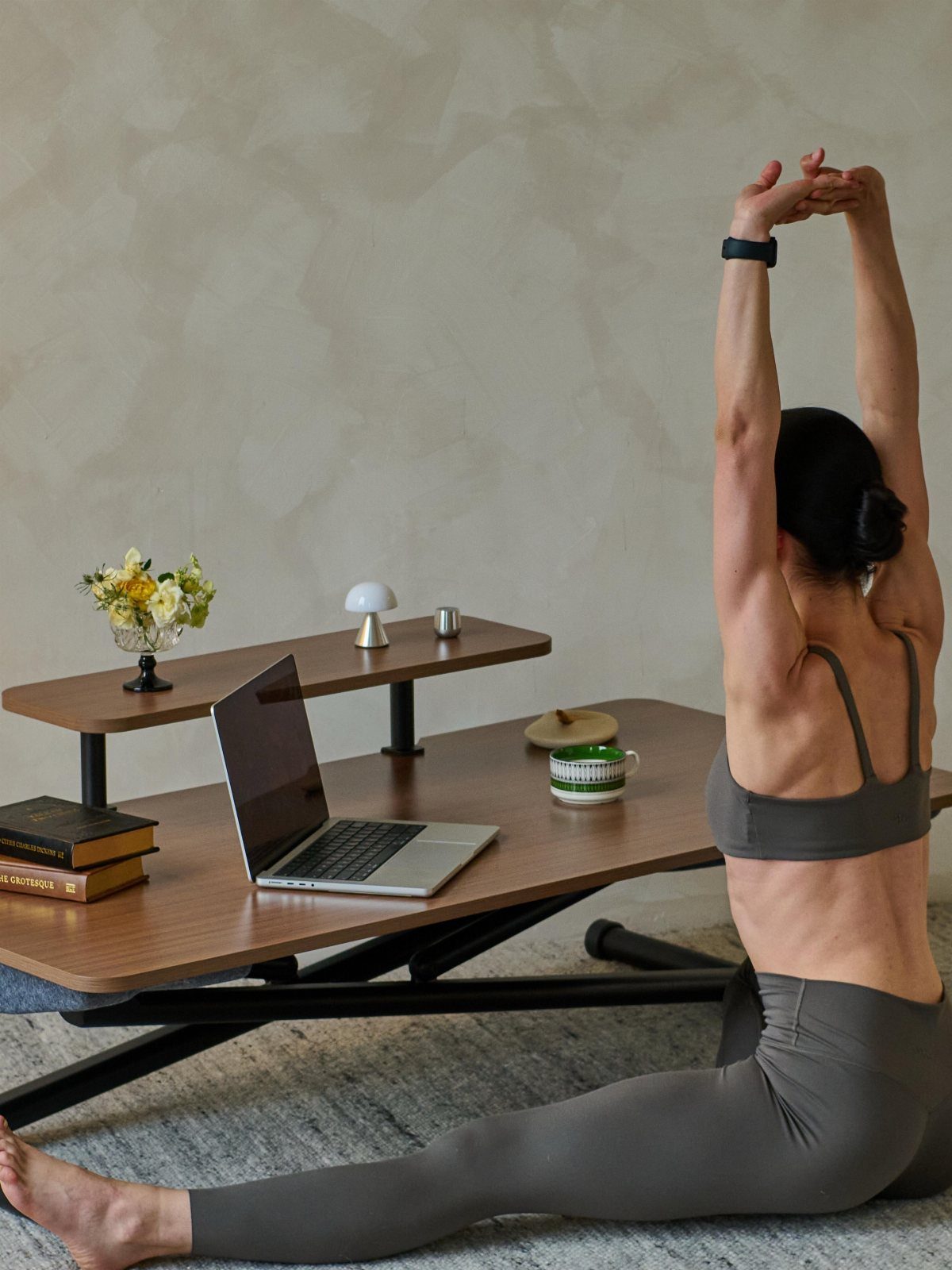 Woman stretching her arms while sitting on the floor beside a wooden desk setup.