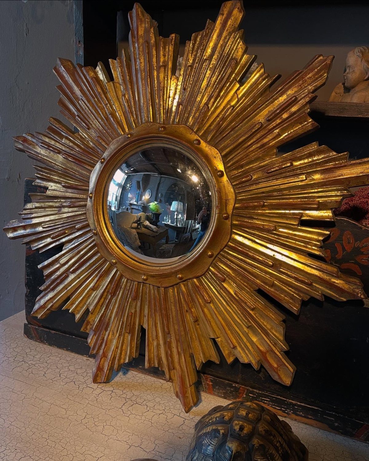 Mirror Wall Art: 25 Ideas from Sunburst to Floor Mirrors 1 Round mirror with a large, radiating gold sunburst frame leaning against dark furniture.