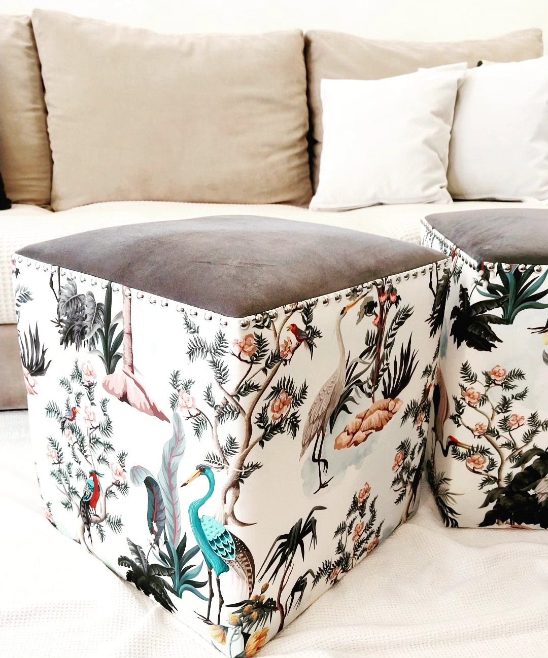 23 Cool House Items for Walls, Shelves, Desks, and Baths 8 Two square fabric poufs with bird prints and grey velvet tops near a sofa.