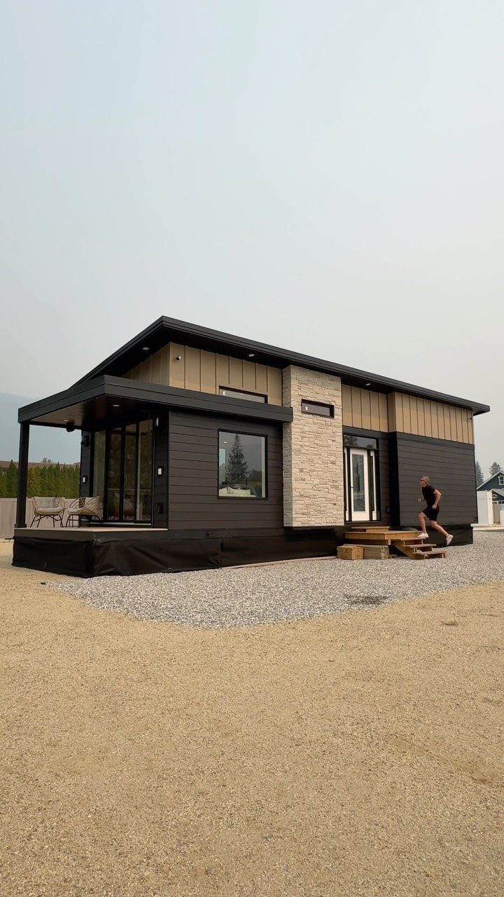 Tiny House Layout Ideas: 34 Kitchens, Lofts, Decks, Porches 23 Modern tiny house with dark grey siding and a small porch on gravel.