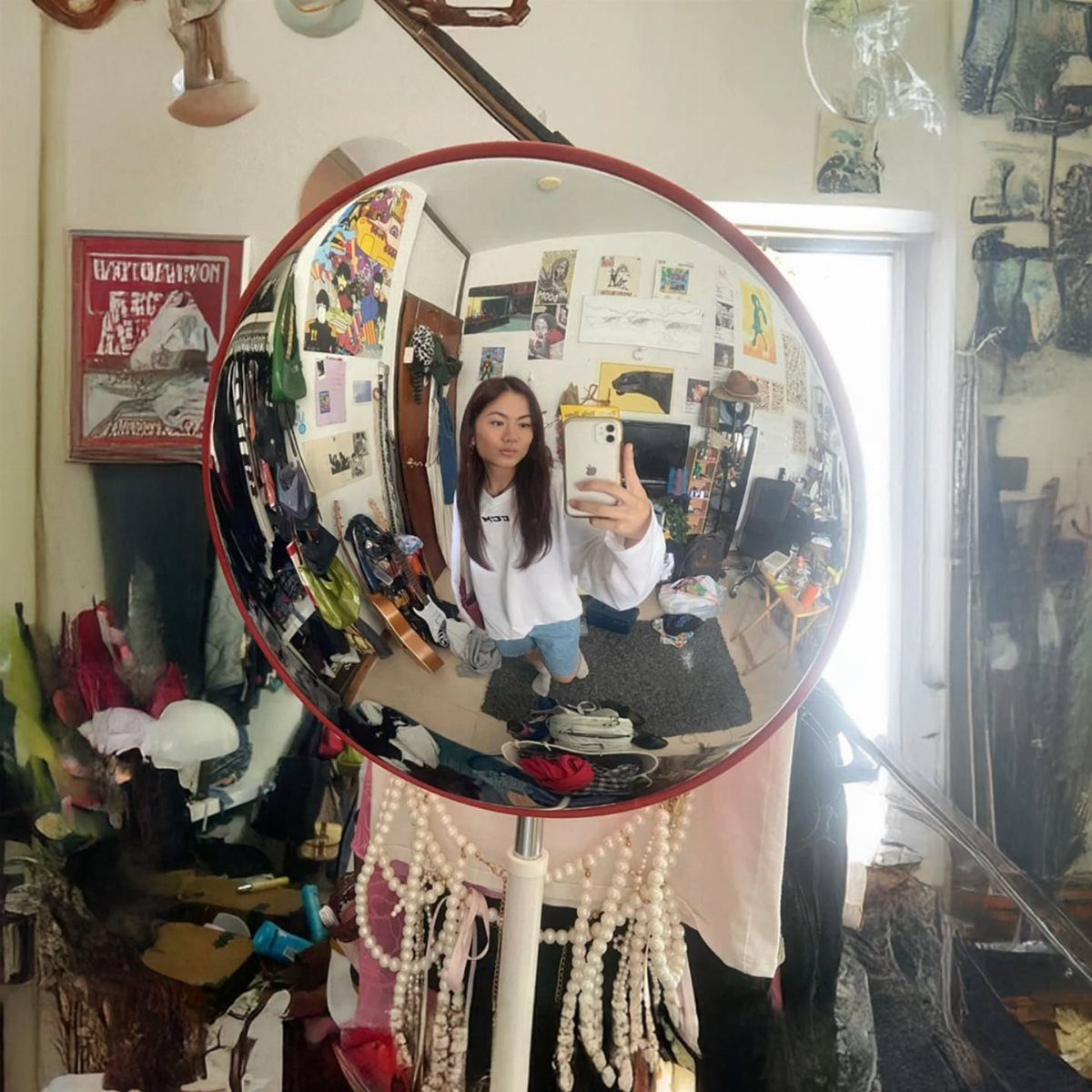 Person taking a selfie in a round convex traffic mirror inside a bedroom.