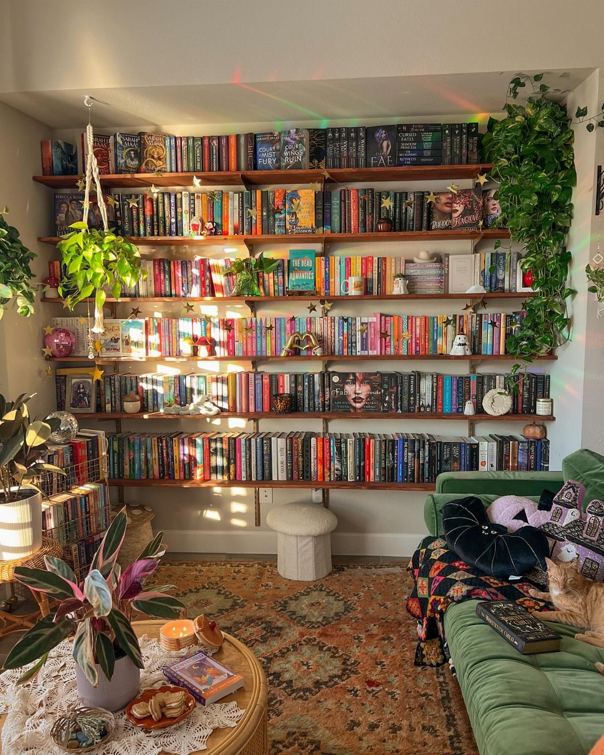 Wooden floating shelves filled with books above a green velvet sofa and patterned rug.