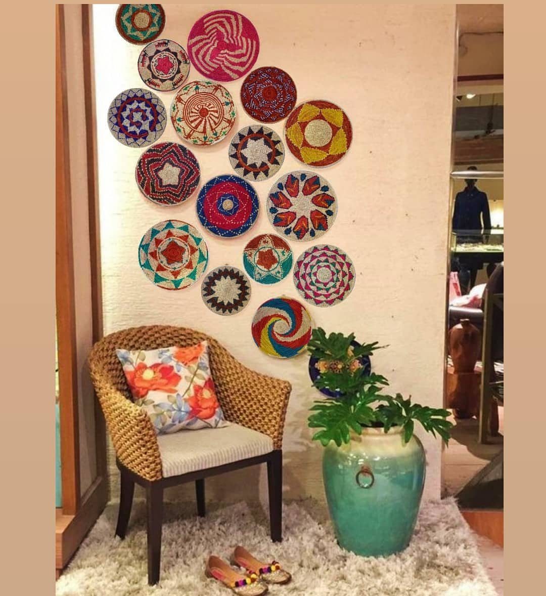 Colorful woven circular baskets hanging on a white wall above a wicker chair.
