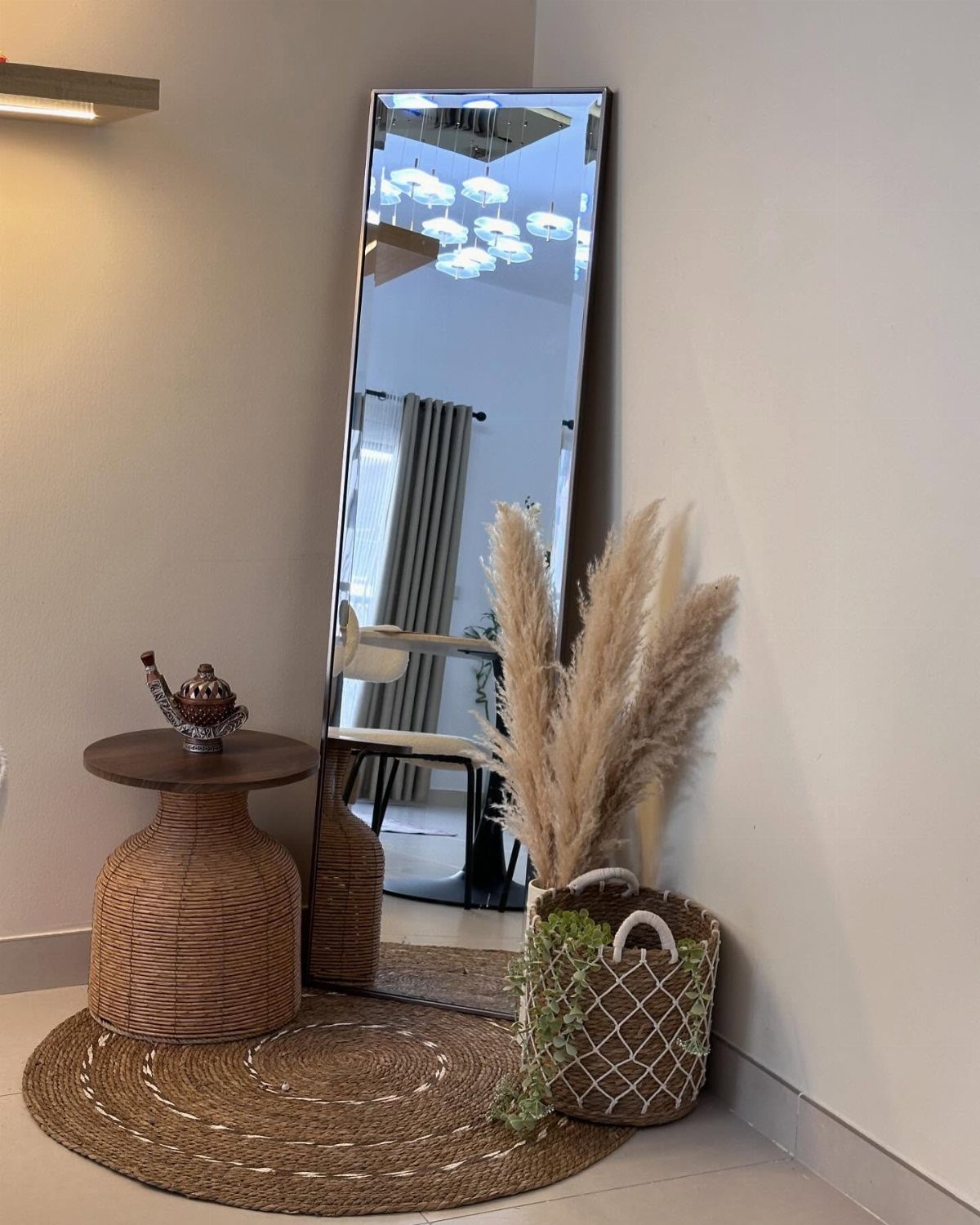 Tall rectangular mirror leaning in a corner with woven furniture and pampas grass.