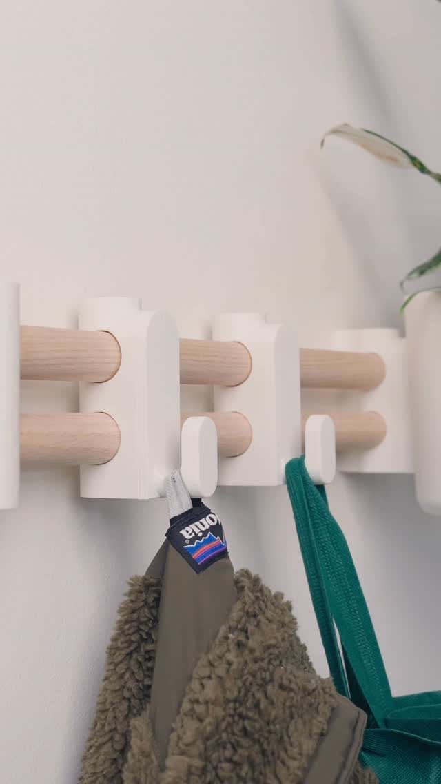 White wall organizer with wooden dowels holding a brown jacket and green strap.