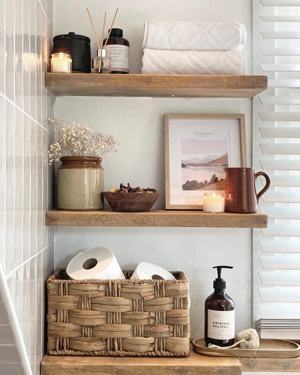 Bathroom Shelf Unit Ideas: 28 Storage and Display Options 25 Wooden floating bathroom shelves holding white towels, woven baskets, and decorative apothecary bottles.