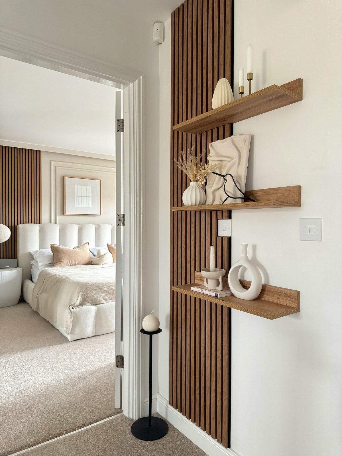 22 Bedroom Empty Wall Ideas, from Gallery Walls to Plaster 17 Vertical wooden wall slats with floating shelves holding white decorative vases and candles.