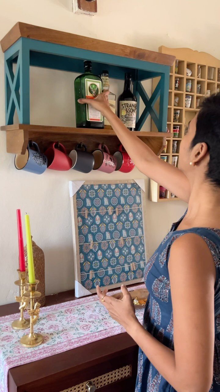 40 Home Decor Item Ideas, From Candle Holders to Sculptures 7 Wall-mounted blue and wooden shelf holding bottles and mugs with a woman reaching.