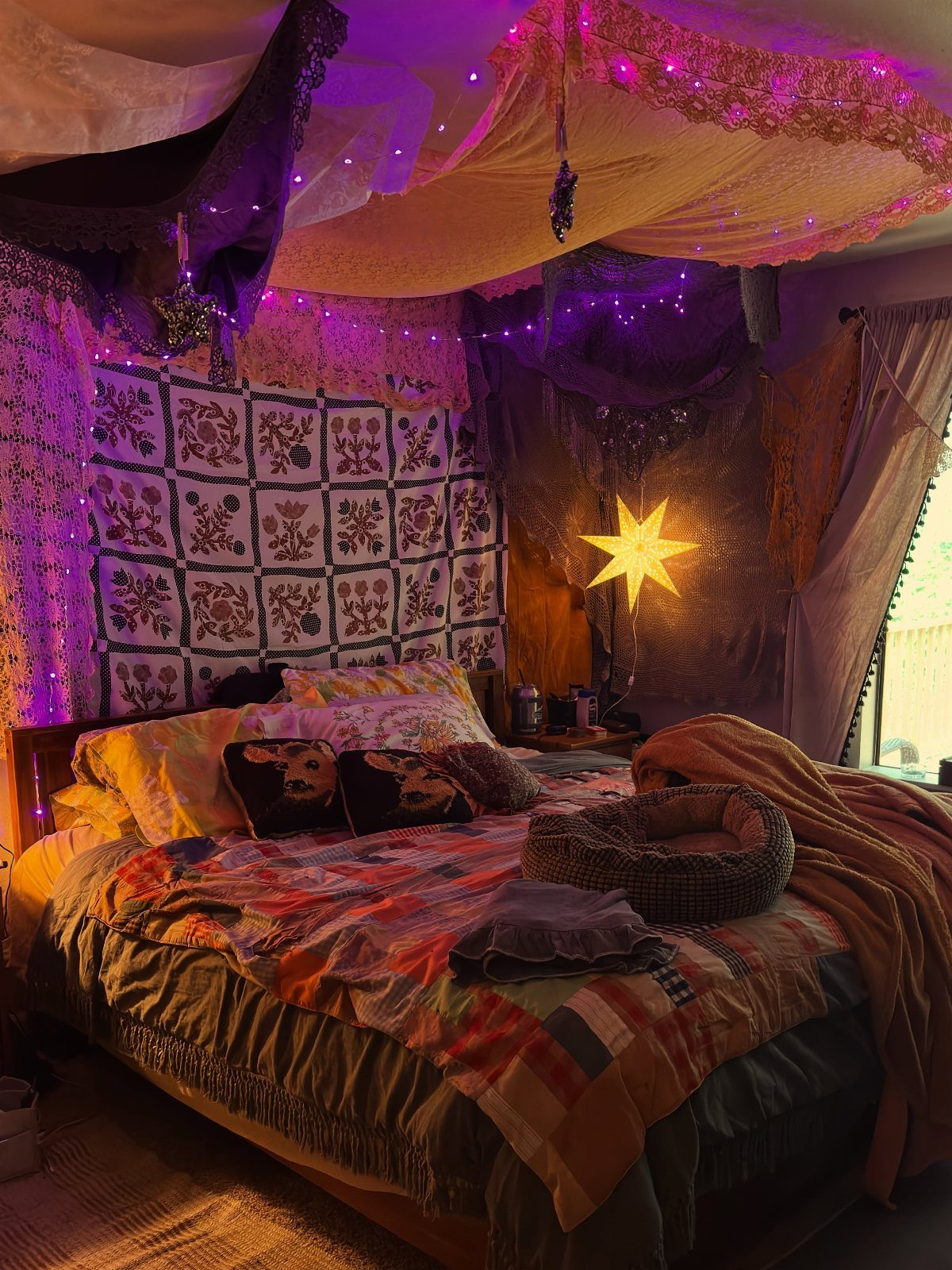13 Alt Room Decor Ideas with Moody Colors, Wood, and Plants 1 Bed with patchwork quilt and brown throw under purple string lights and canopies