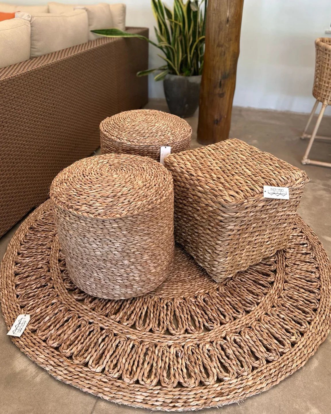 Wicker storage ottomans of various shapes on a circular jute rug in a living room.