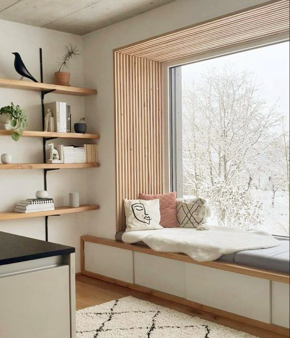 Built-in window bench with white storage drawers and pillows overlooking a snowy scene.
