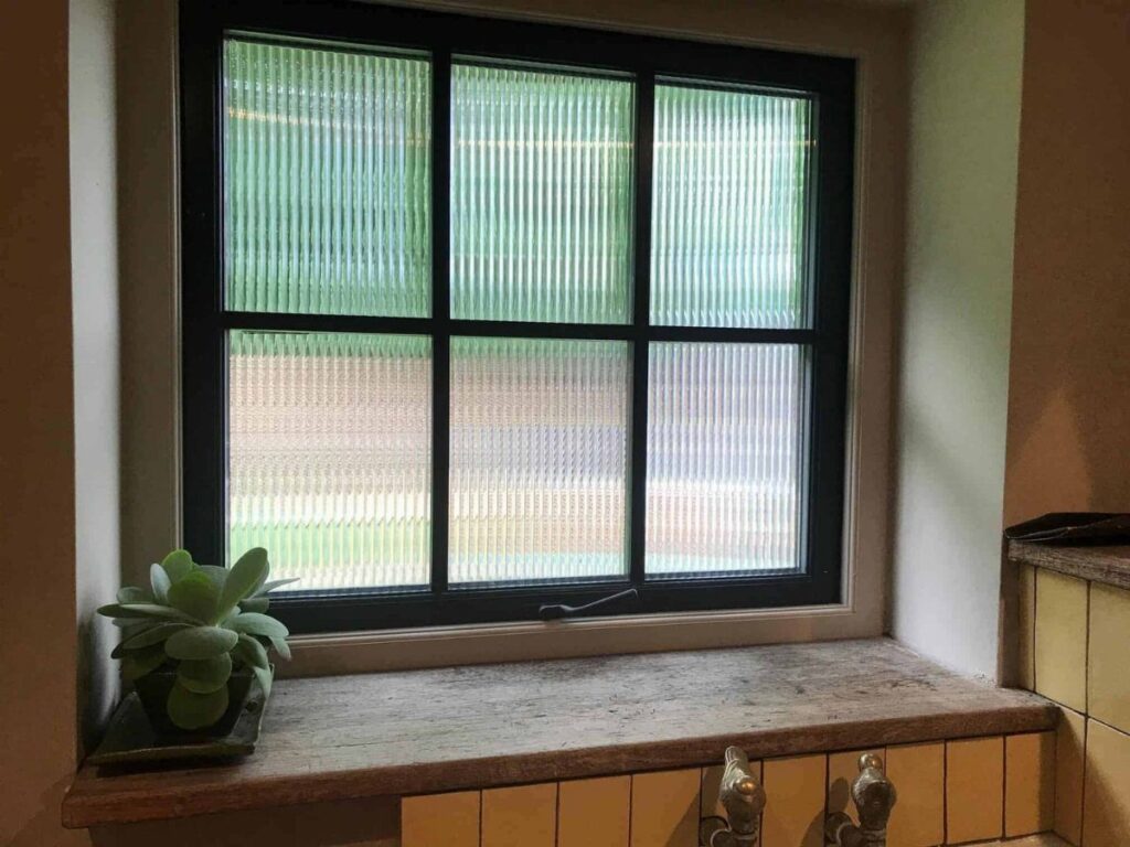 Black framed window with ribbed privacy film and a small succulent on the ledge