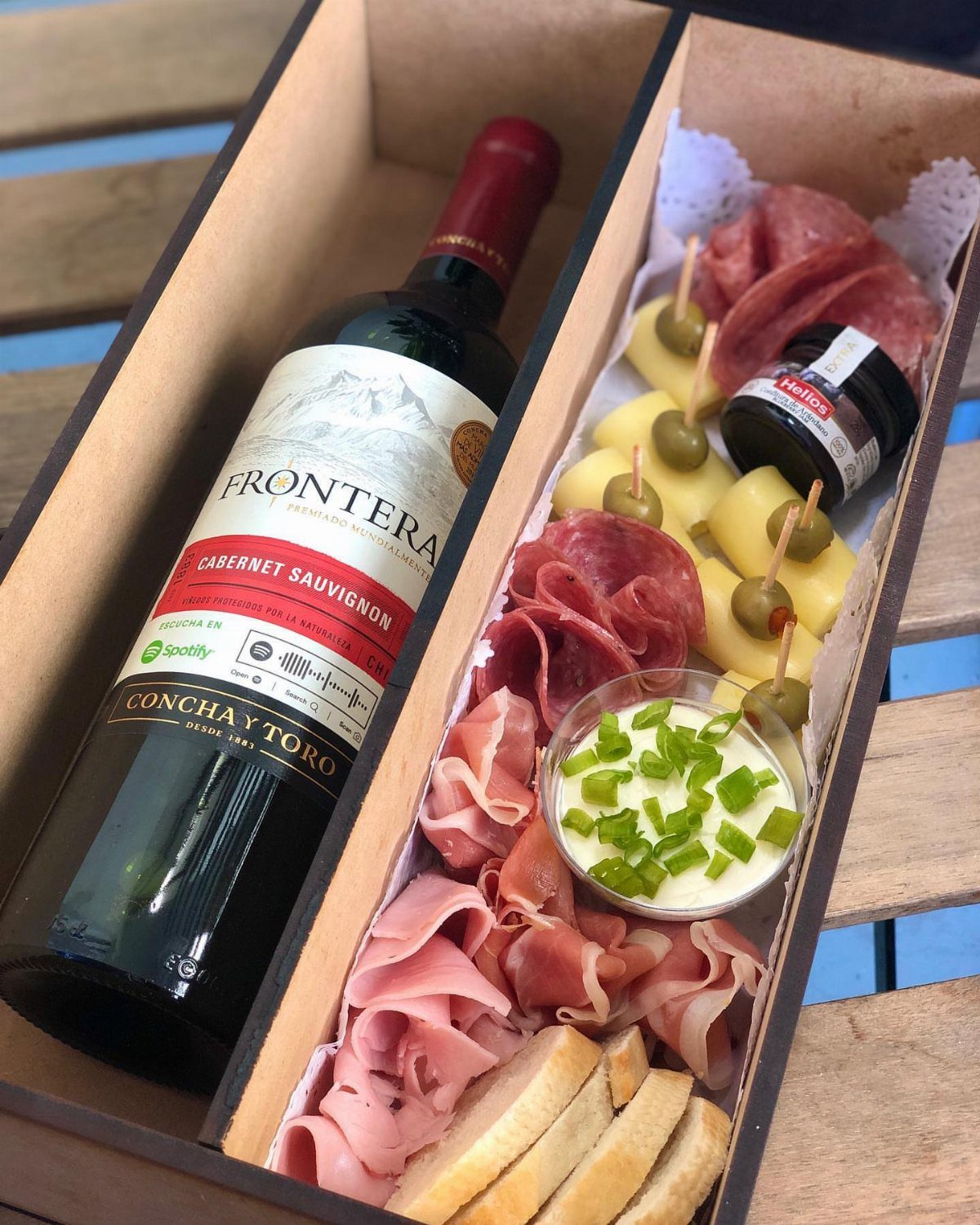 Wine and cheese gift box with red wine, charcuterie, olives, and sliced baguette.